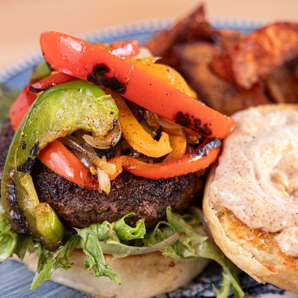Milque Toast's breakfast burger with grilled peppers, onions, lettuce, and a side of potato wedges.