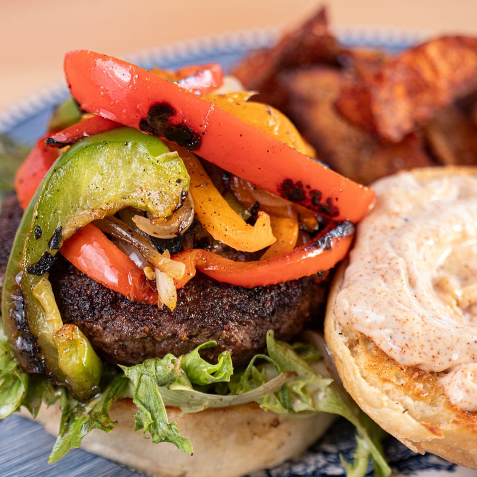 Milque Toast's breakfast burger with grilled peppers, onions, lettuce, and a side of potato wedges.