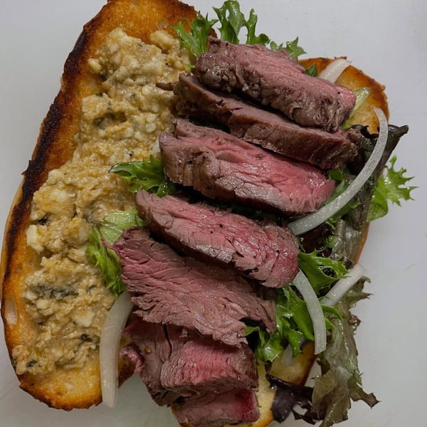 Milque Toast's steak sandwich with rare beef, lettuce, onions, and a creamy spread on toasted bread.