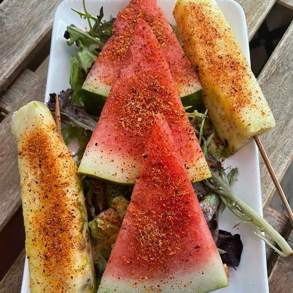 Watermelon slices and pineapple spears, seasoned with chili powder, on a bed of greens.