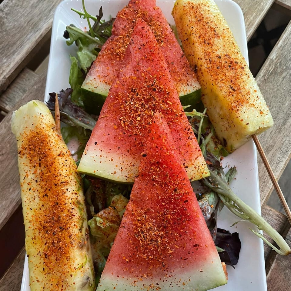Watermelon slices and pineapple spears, seasoned with chili powder, on a bed of greens.