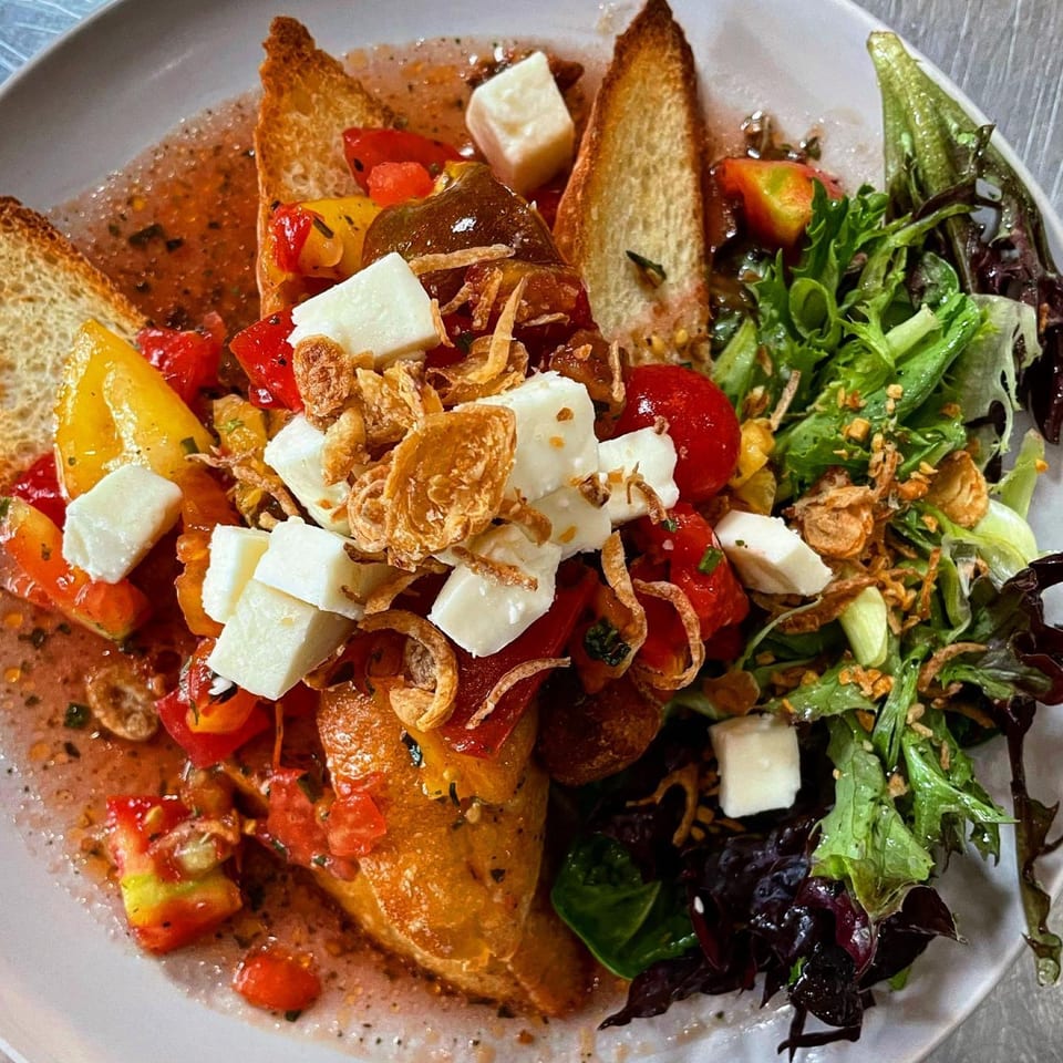 Milque Toast's breakfast dish with toasted bread, diced tomatoes, cheese cubes, and a side salad.