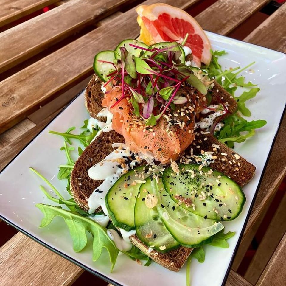 Milque Toast's salmon toast with cucumber, microgreens, and a grapefruit slice on a wooden table.