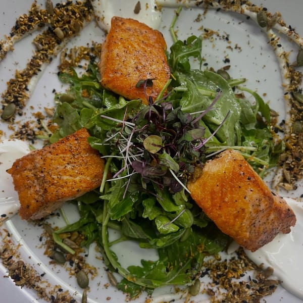 Three pieces of seared salmon on a bed of arugula, garnished with microgreens and seeds.