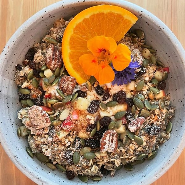 Milque Toast's oatmeal bowl with nuts, seeds, dried fruit, orange slice, and edible flowers.