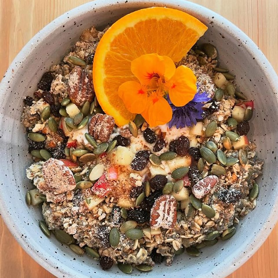 Milque Toast's oatmeal bowl with nuts, seeds, dried fruit, orange slice, and edible flowers.